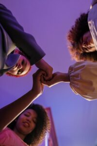 Three black women standing together, holding hands in unity against a purple background.