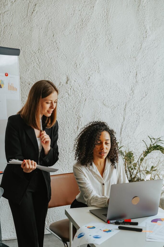 Mastering the First Impression: Your intriguing post title goes here Two businesswomen sharing ideas on a project, working together on a laptop in a modern office setting.